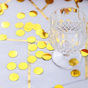 May include: A clear glass goblet with a diamond pattern sits on a white tablecloth with gold confetti scattered around it.