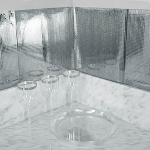 May include: Clear plastic wine glasses with silver rims and a matching serving tray. The glasses and tray are arranged on a white marble surface, with a mirrored tile backsplash in the background.