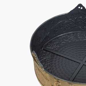 May include: A black metal cake pan with a gold rim and intricate floral design. The pan has a removable bottom and a cross-shaped support inside.