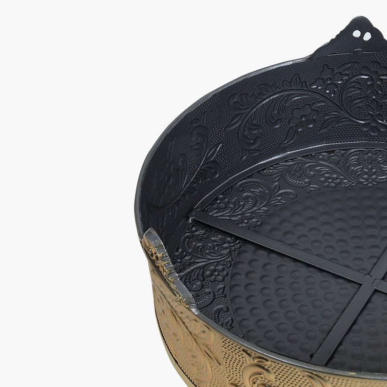 May include: A black metal cake pan with a gold rim and intricate floral design. The pan has a removable bottom and a cross-shaped support inside.