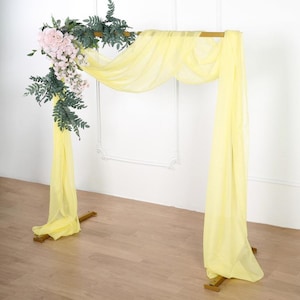 May include: A gold metal archway decorated with a yellow sheer fabric backdrop and a garland of pink flowers and green leaves.