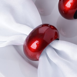 May include: Red wooden napkin rings. The rings are smooth and glossy. They are perfect for adding a touch of elegance to any table setting.