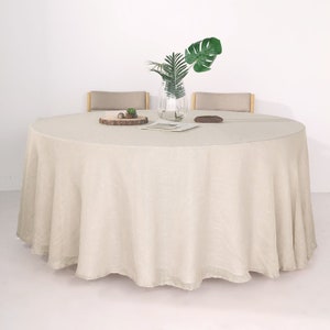 May include: A round, off-white linen tablecloth draped over a table with two chairs. A small potted plant sits on a wooden coaster in the center of the table.