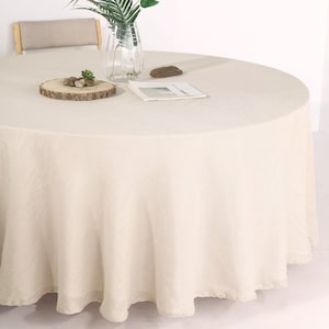 May include: A round, off-white tablecloth with a subtle texture. The tablecloth is draped over a round table and has a slight ruffle around the edge.