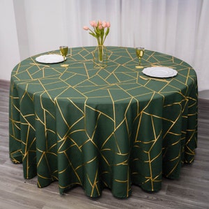 May include: A round green tablecloth with a gold geometric pattern. The tablecloth is laid out on a wooden table with two glasses and plates on top.