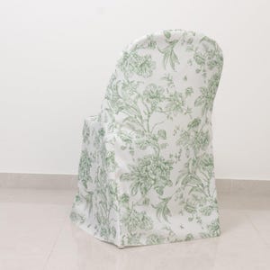 May include: A white chair cover with a green floral pattern. The cover is draped over a chair, showcasing a classic botanical design. The fabric has a soft, textured appearance, adding a touch of elegance to the chair.