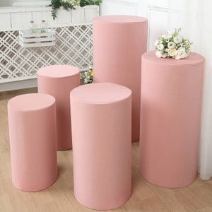 May include: Set of four pink cylindrical display stands of varying heights. The stands are made of a smooth, fabric-like material and are perfect for showcasing products or decorations.