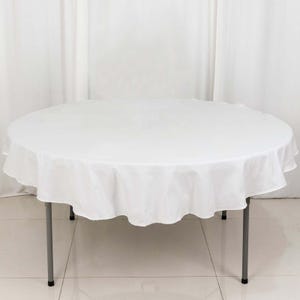 May include: A round white tablecloth draped over a metal folding table. The tablecloth has a scalloped edge and hangs to the floor. The table legs are gray and the floor is tiled.