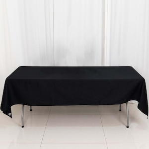 May include: A black rectangular tablecloth draped over a folding table with silver legs. The tablecloth covers the entire table, with the edges hanging down. The background is a white curtain.