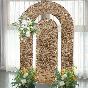May include: A gold sequin archway with a rectangular center and an arched top. The arch is decorated with white and yellow flowers at the top and bottom. The background is a sheer white curtain.