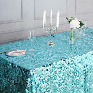 May include: A turquoise sequin tablecloth with a silver candelabra and a vase of white flowers on top. The tablecloth is made of a soft, shimmery fabric and is perfect for adding a touch of glamour to any event.