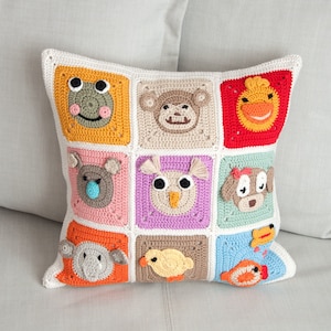 Könnte beinhalten: Ein gehäkeltes Kissen mit weißem Hintergrund und neun bunten Quadraten mit verschiedenen Tiergesichtern. Die Tiere sind ein Frosch, ein Affe, eine Ente, ein Koala, eine Eule, ein Hund, ein Elefant, ein Küken und ein Fisch.