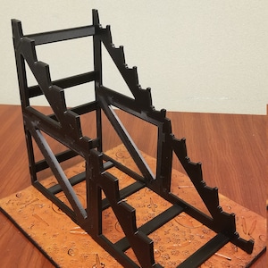 May include: Black plastic stand with multiple tiers for displaying items. The stand is on a brown surface with a patterned design.