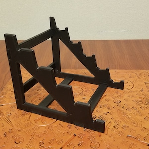 May include: Black plastic display stand with five tiers for displaying small items.