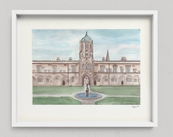 May include: A watercolor painting in a white frame depicting a stone building with a central tower, arched walkways, and a blue-domed roof. A circular fountain sits in the center of a green lawn in front of the structure under a pale blue sky.