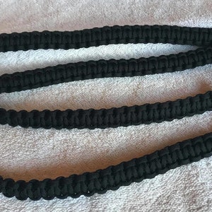 Op de afbeelding: Drie zwarte paracord-riemen met zilveren metalen gespen en een ring. De riemen zijn gevlochten en hebben een textuur.