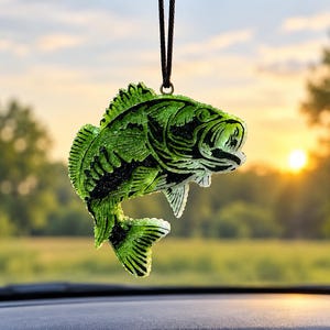 May include: A translucent lime green and black fish-shaped hanging ornament with a textured, crystalline surface. The fish is suspended by a thin black cord, featuring detailed fin and scale patterns with a prominent open mouth design.