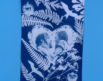 Op de afbeelding: Een blauw-witte print met een stel dat elkaar omhelst in een hartvormige lijst. De afbeelding is omgeven door witte botanische illustraties, waaronder varens en vogels. Het ontwerp heeft een vintage, romantische uitstraling.