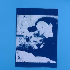 Peut inclure: Une impression pli&eacute;e, bleu fonc&eacute;, sur un fond bleu clair. L'impression pr&eacute;sente une image blanche et bleu fonc&eacute; d'un visage et d'un chien. L'image est une repr&eacute;sentation artistique &agrave; fort contraste.