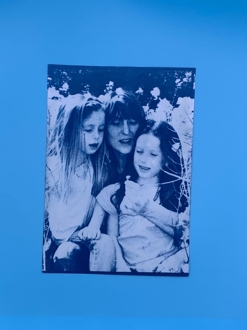 Peut inclure: Photographie en noir et blanc de trois personnes, probablement une m&egrave;re et deux enfants, en ext&eacute;rieur. L'image est imprim&eacute;e sur un papier rectangulaire, avec un fond bleu.