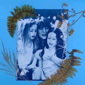 Peut inclure: Photographie en tons bleus d'un portrait de famille, avec une m&egrave;re et deux enfants. L'image est encadr&eacute;e de plantes et de fleurs s&eacute;ch&eacute;es, sur un fond bleu clair. La photo est un portrait d'une m&egrave;re et de deux enfants.