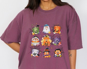 May include: A maroon t-shirt featuring a colorful Halloween-themed graphic. The graphic includes various cartoon characters such as a ghost, pumpkin, and vampire. The shirt is a relaxed fit.