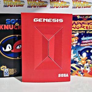 May include: Three SEGA Genesis video game boxes. The boxes are red, black, and blue. The boxes feature the SEGA logo and game titles like "Sonic & Knuckles" and "Wacky Worlds Creativity Studio". The red box has the word "GENESIS" in white.