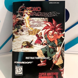 Puede incluir: Folleto de instrucciones de Chrono Trigger para Super Nintendo. La portada presenta una vibrante ilustraci&oacute;n de personajes en un paisaje nevado, con el t&iacute;tulo del juego en un lugar destacado. El folleto est&aacute; clasificado para mayores de 6 a&ntilde;os.
