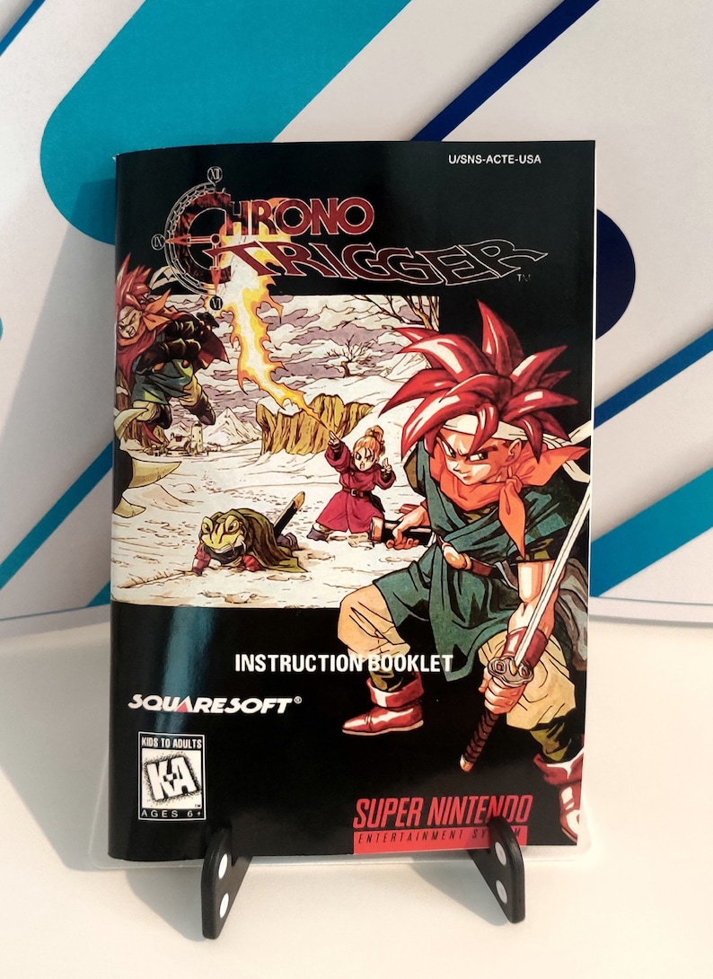 Puede incluir: Folleto de instrucciones de Chrono Trigger para Super Nintendo. La portada presenta una vibrante ilustraci&oacute;n de personajes en un paisaje nevado, con el t&iacute;tulo del juego en un lugar destacado. El folleto est&aacute; clasificado para mayores de 6 a&ntilde;os.