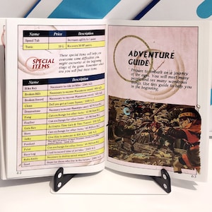 Puede incluir: Un libro abierto sostenido por un atril negro. La p&aacute;gina izquierda presenta una lista de "Art&iacute;culos especiales" con detalles. La p&aacute;gina derecha muestra una "Gu&iacute;a de aventuras" con una ilustraci&oacute;n de una escena de batalla.