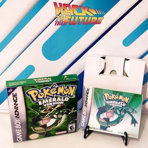 Może przedstawiać: Zielone pudełko na kartridż gry Game Boy Advance z tekstem "Pokémon wersja Szmaragd" i zielono-czarnym obrazkiem Pokemona na przodzie. Pudełko znajduje się obok białego pudełka na kartridż gry Game Boy Advance z zielono-czarnym obrazkiem Pokemona na przodzie. Tekst "Pokémon wersja Szmaragd" znajduje się na przodzie pudełka. Tekst "Instrukcja" znajduje się na przodzie pudełka.