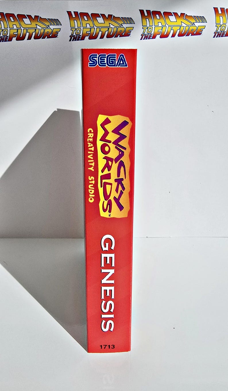 K&ouml;nnte beinhalten: Rote SEGA Genesis-Spielh&uuml;lle mit dem Spiel "Wacky Worlds Creativity Studio". Das Geh&auml;use zeigt das SEGA-Logo und das Wort "Genesis" vertikal. Der Spieletitel ist in Gelb und Lila.