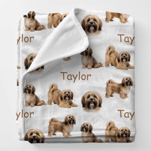 May include: White blanket featuring a repeating pattern of brown Havanese dogs in various poses. The word "Taylor" is printed in brown on the blanket. The blanket is folded over, revealing the white underside.
