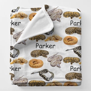 May include: White blanket featuring various colorful snake illustrations. The word "Parker" is printed in black on the blanket. The snakes are in shades of brown, yellow, and gray.