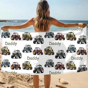 May include: White beach towel featuring a repeating pattern of colorful tractors. The tractors are in various colors, including green, orange, and yellow. The word "Daddy" is printed in green on the towel.