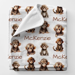 May include: White plush blanket featuring a repeating pattern of adorable brown baby monkeys. The name "McKenzie" is printed in brown script across the blanket. The blanket is soft and cozy, perfect for a nursery or child's room.