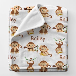 May include: White blanket with a repeating pattern of cartoon monkeys in various poses, holding bananas and vines. The name "Bailey" is printed in brown on the blanket. The monkeys are brown with tan faces.