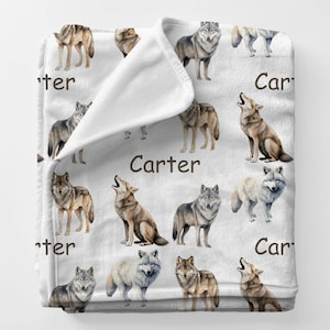 May include: White fleece blanket featuring a repeating pattern of watercolor wolves in various poses and colors. The word "Carter" is printed in brown on the blanket. The blanket is folded over, showing the soft texture.