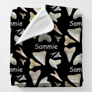May include: Black blanket with a pattern of shark teeth in various sizes and shades of white and tan. The name "Sammie" is printed in white on the blanket.