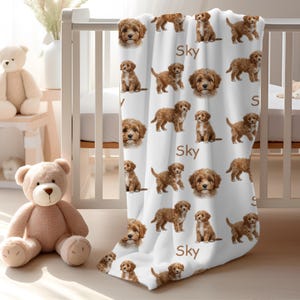 K&ouml;nnte beinhalten: Wei&szlig;e Babydecke mit einem sich wiederholenden Muster aus braunen Welpen und dem Wort "Sky". Die Decke ist &uuml;ber ein wei&szlig;es Kinderbett drapiert. Zwei Teddyb&auml;ren befinden sich im Vordergrund.