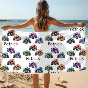 May include: A white beach towel featuring colorful ATV illustrations in red, green, blue, purple, and gold. The word "Patrick" is printed on the towel. The towel is being held up on a beach with the ocean in the background.