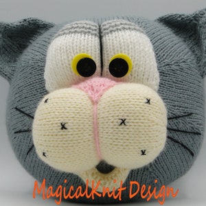 May include: A gray knitted cat head with white and pink facial features, black eyes with yellow pupils, and black whiskers.