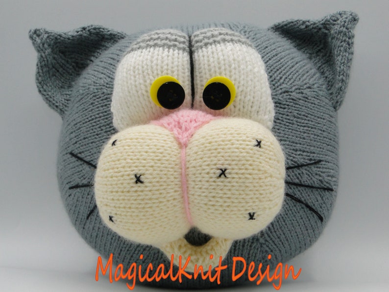 May include: A gray knitted cat head with white and pink facial features, black eyes with yellow pupils, and black whiskers.