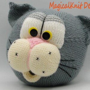 May include: A gray knitted cat head with white and gray stripes, yellow eyes, a pink nose, and black whiskers. The cat head is a knitted toy.