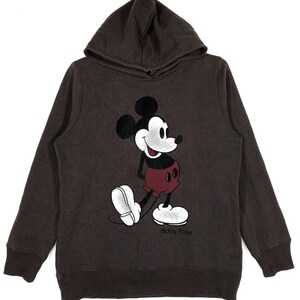May include: A brown hooded sweatshirt featuring a vintage-style Mickey Mouse graphic on the front. The graphic is in black, white, and red. The text "Mickey Mouse" is printed below the graphic.