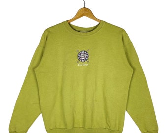Puede incluir: Una sudadera de color verde lima con un gráfico de una cara de sol con el texto "San Diego" debajo.