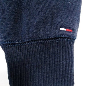 May include: Close-up of the navy blue ribbed cuff of a sweatshirt with a small white and red logo on the fabric.