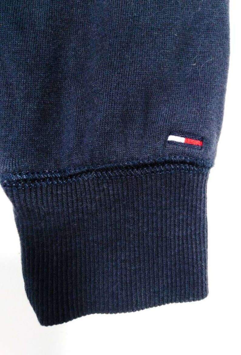 May include: Close-up of the navy blue ribbed cuff of a sweatshirt with a small white and red logo on the fabric.
