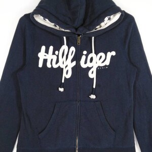 May include: A navy blue zip-up hoodie with a white "Hilfiger Denim" logo on the front. The hoodie has a white star pattern on the inside of the hood.