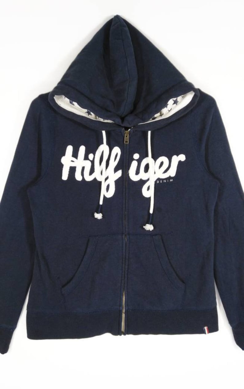 May include: A navy blue zip-up hoodie with a white "Hilfiger Denim" logo on the front. The hoodie has a white star pattern on the inside of the hood.